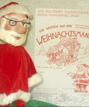 Foto von der Weihnachtsmann-Marionette vor dem Plakat zum Stück.