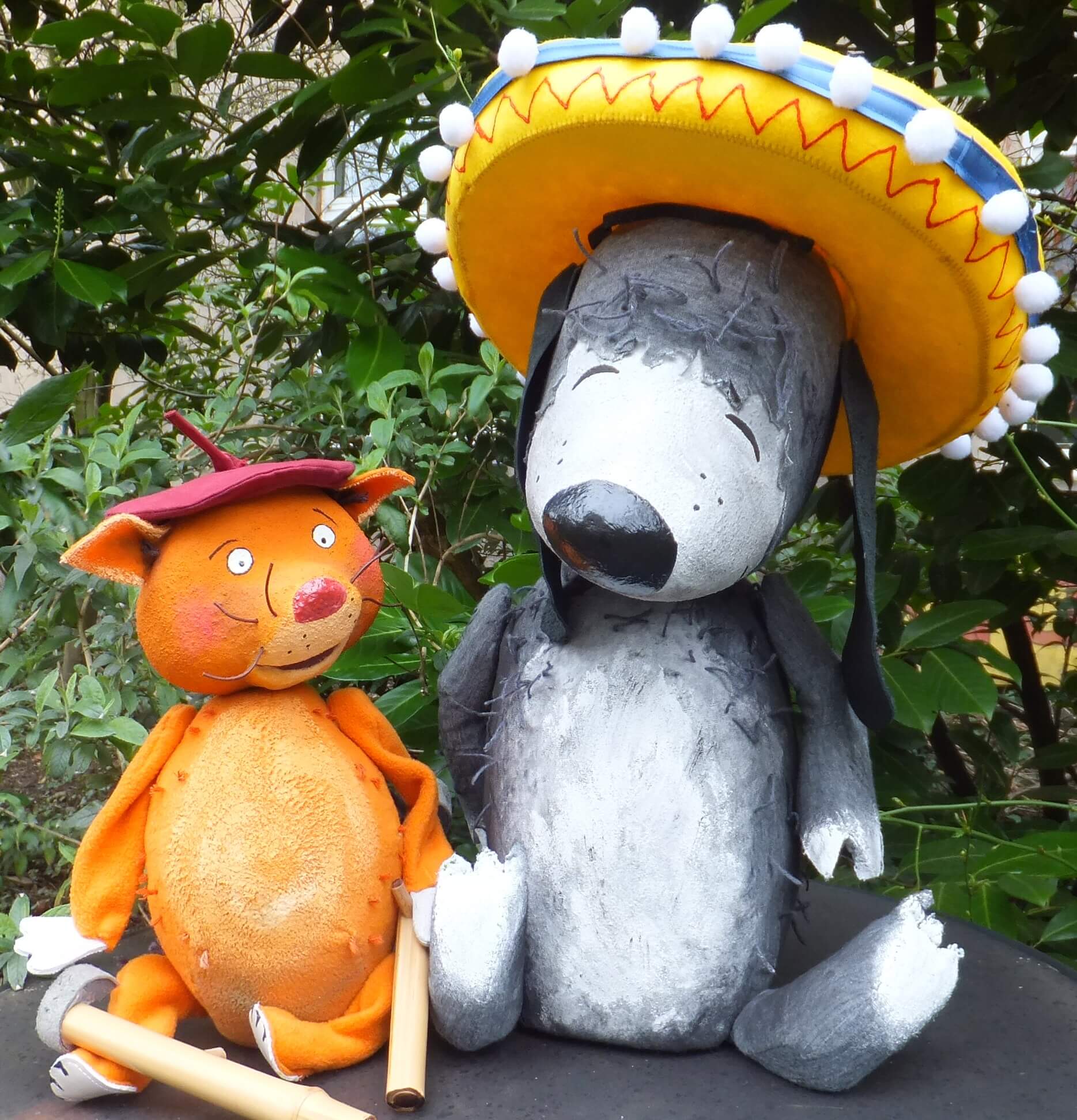 Foto: Die Katze Rosalie mit einer Baskenmütze auf dem Kopf und der Hund Pedro, welcher einen großen Hut (Sombrero) trägt.