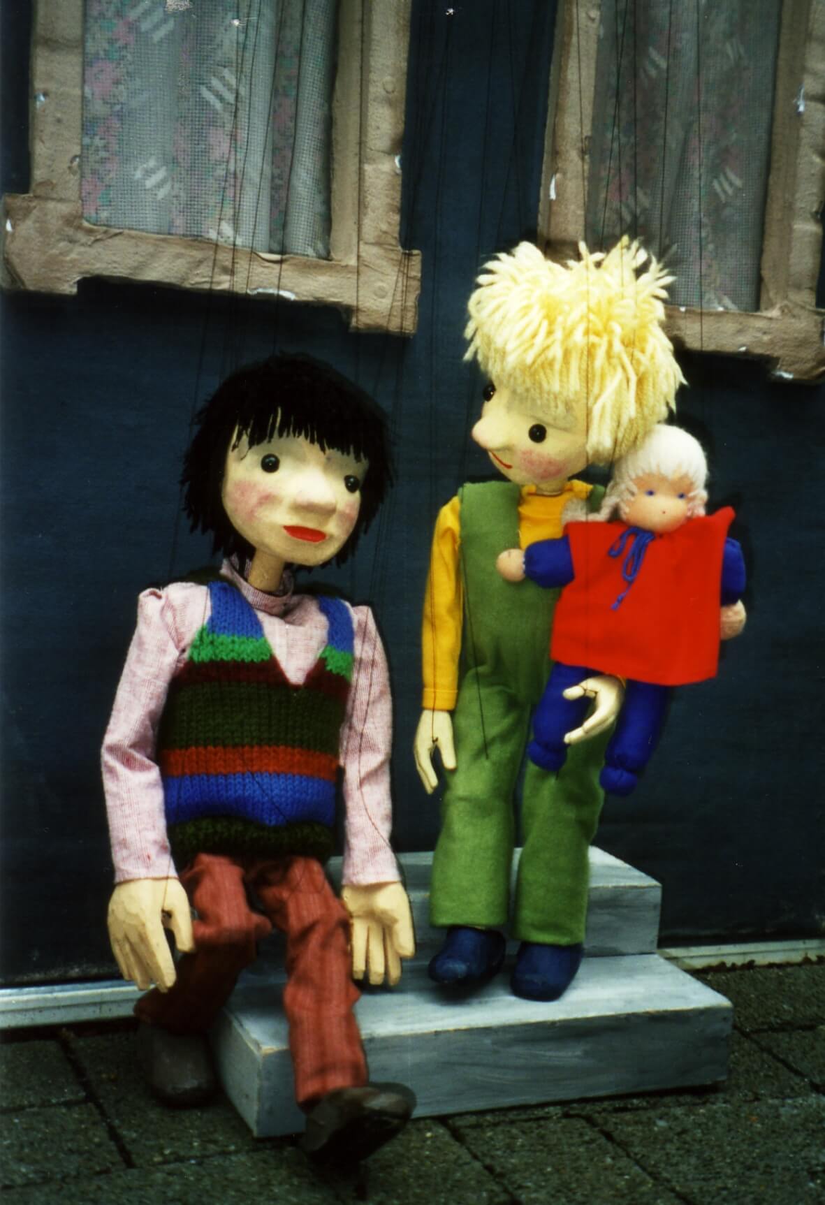 Foto: Selim und und Susanne sitzen auf einer Treppe. Susanne hat eine Puppe in der Hand