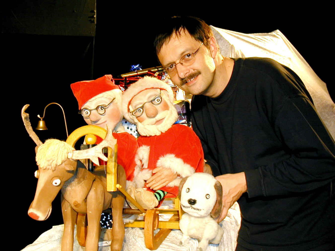 Foto: Der Weihnachtsmann und seien Frau sitzen in einem Rentierschlitten. Daneben sitzt ein Hund. Rechts im Bild Wolfgang Kaup-Wellfonder