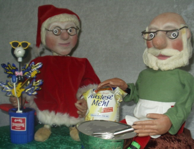 Foto: Der Weihnachtsmann und seine Frau backen Kekse. Auf dem Tisch steht eine Rührschüssel und Mehl