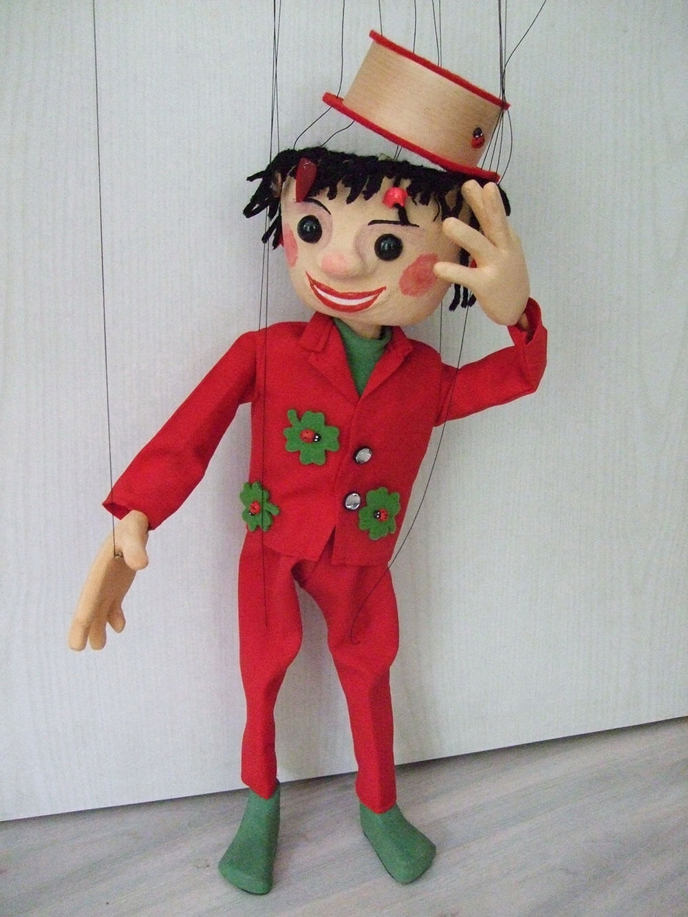Freundlich lächelnde Marionette mit rotem Anzug mit aufgenähten Glückskleeblättern. In dem Hut können Geschenke „versteckt” werden. 